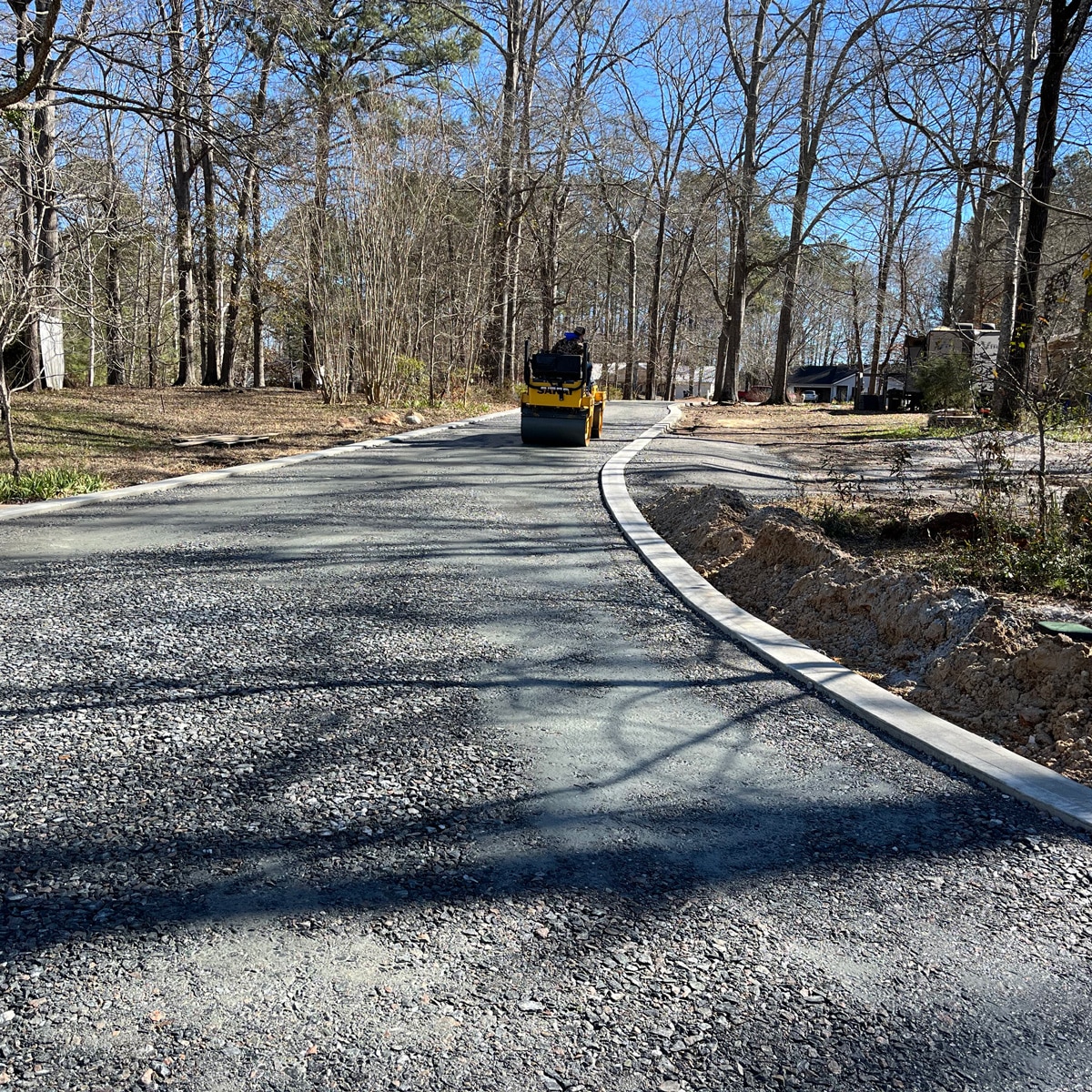 man riding on paving roller machine over freshly paved residential driveway